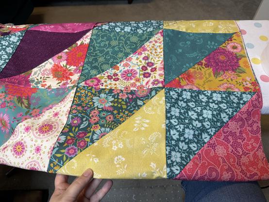 A hand holding up a quilt top made of six large (9.5”) half-square triangles sewn together in bright patterns.