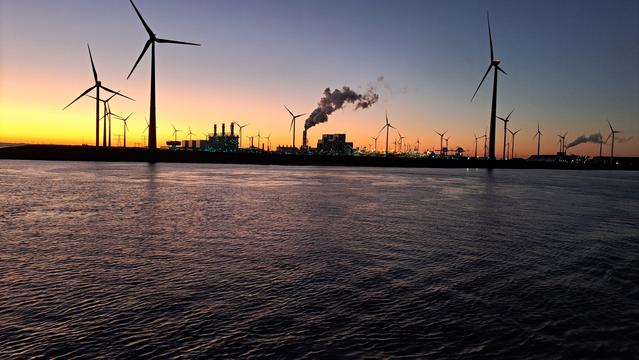 Eemshaven, NL sunset
"A number of power plants operate at the site. Both Electrabel and NUON operate a gas-fired power plant there while RWE Innogy operates a wind farm at the site. RWE is operating a coal-fired plant." A sunset that paints the deep blue sky in vibrant colors: seamlessly transitioning from pink and orange to yellow. This contrasts with the turquoise and blue lights of the power plants, photographed from the sea. The sea in the foreground, rippled by tiny waves, shimmers in blue and pink. The wind turbines of a wind farm contrast with the colourful sky.
The wall of one of the power plants appears bright pink.