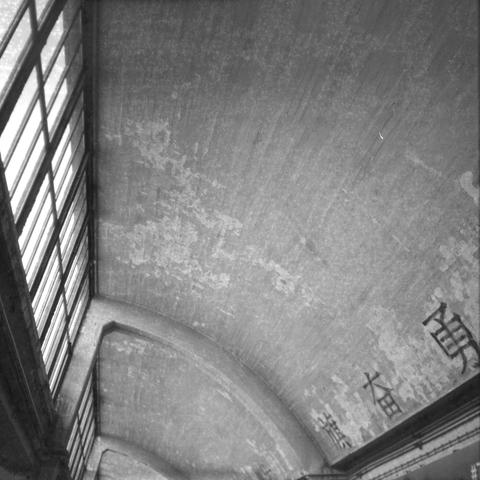 Ilford HP5 Plus 400 (6x6)
English Alt Text: A black and white image captures the interior of a large building with an arched ceiling and tall windows on the left. The ceiling appears weathered, with visible streaks and patches. On the right wall near the ceiling, large Chinese characters are painted, suggesting cultural or historical significance. The architecture hints at a public space, possibly a train station or hall in a Chinese-speaking region.
中文替代文字: 这是一张黑白照片,展示一座大型建筑的内部,拱形天花板高耸,左侧排列着高窗。天花板表面斑驳,有明显的痕迹和斑点。右侧墙面靠近天花板处绘有大型中文字符,暗示该地具有文化或历史意义。建筑风格表明这可能是一个公共场所,如车站或中国地区的大厅。