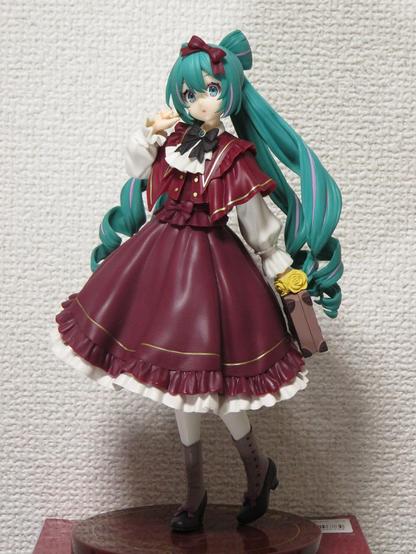 A figurine for amusement arcades: "Trio-Try-iT: Hatsune Miku, Classical Retro" by Furyu.
A young woman, standing on the circular base, holding a classical square bag on her left hand, with a soft shawl, a long skirt, etc in Maroon color and long curled peppermint green pigtails.