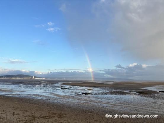 A photograph of Swansea Bay with the city of Swansea in the background. A passing storm and a double rainbow appear in the picture.