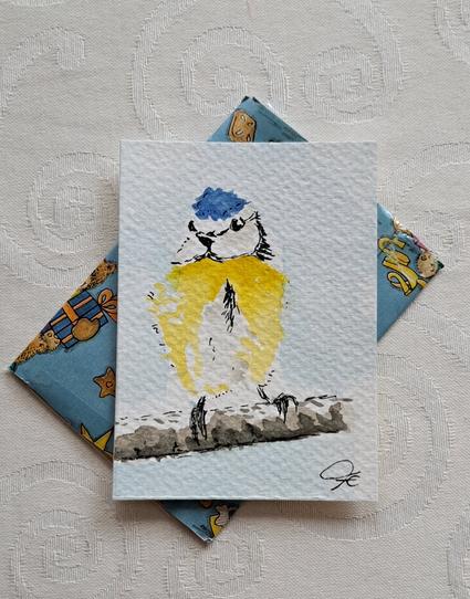 ATC im Hochformat, Aquarell: Eine Blaumeise mit blauer Haube und gelbem Bauch sitzt auf einem Ast, von vorne gesehen. Künstlermonogram unten rechts.