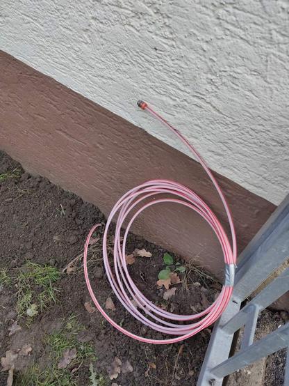ein rot-weißes Glasfaser Kabel im Freien neben einer Hauswand