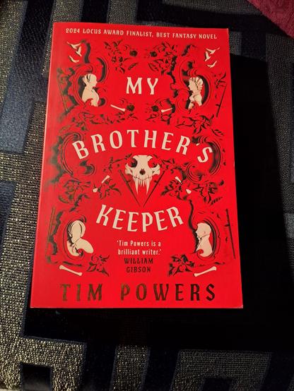 The cover of the book. 

An animal skull with two sabre-like teeth is in the middle of the image, with four cameo-like images of people in the corners. There are bones and daggers in decoration, and curling stone-like leaves.