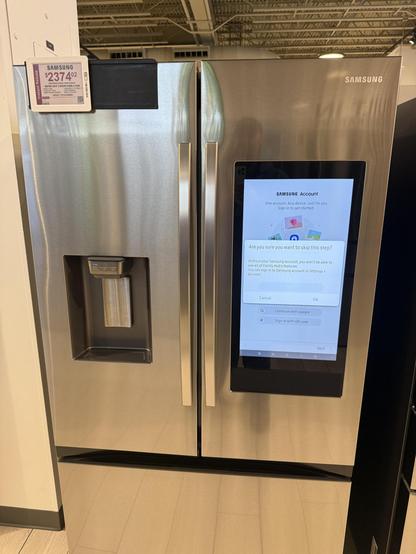 Stainless steel side-by-side Samsung refrigerator with a gigantic iPad, looking thing covering almost the entire entirety of one of the half panels. It’s already showing an error message.