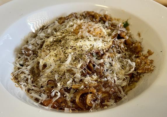 a bowl full of fresh hand-cut pasta absolutely swimming in a rich thick dark red sauce, which has been topped with herbs and pepper and shredded grana padano. there is also a fried egg buried under that stuff too.