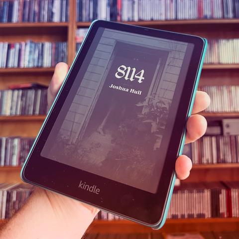An image of a hand holding a Kindle e-reader displaying the book "8114" by Joshua Hull. In the background, shelves filled with CDs are visible.