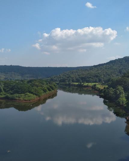 A serene river reflects fluffy white clouds and lush green hills under a clear blue sky.