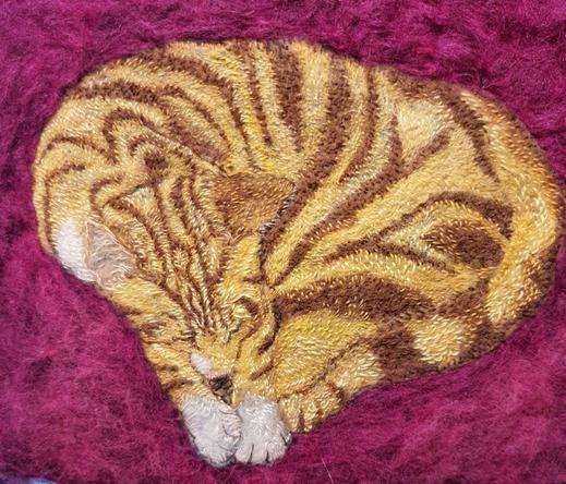 An ambroidered picture of a ginger and white cat curled up.