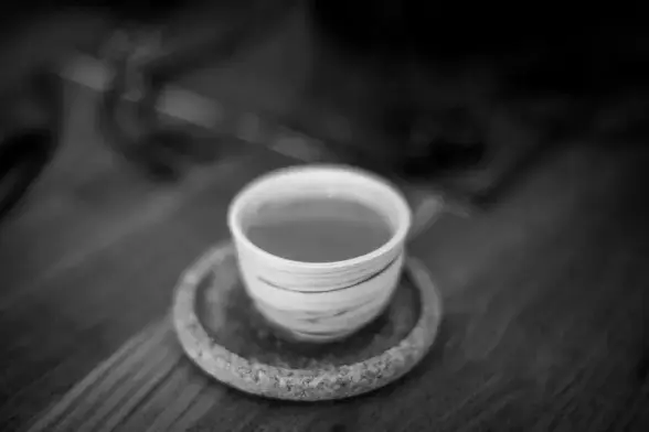 Ein Schwarz-Weiß-Foto einer kleinen Teetasse auf einem Untersetzer aus Kork. Der Hintergrund des Bildes ist aufgrund der Tiefenunschärfe nicht zu erkennen.