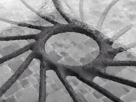 Close-up black-and-white shot of a circular metal structure under rainwater on a textured tabletop, forming a radiating pattern.