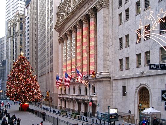 New Yorkin Wall St joulukoristeluissa. Pylväikkö on valaistu jouluvaloilla jotka muodostavat Yhdysvaltain lipun. Pylväikön edessä on suuri kirkkaasti ja värikkäästi valaistu joulukuusi. Rakennuksen edessä on ihmisiä ottamassa kuvaa siitä tai matkakumppaneista.