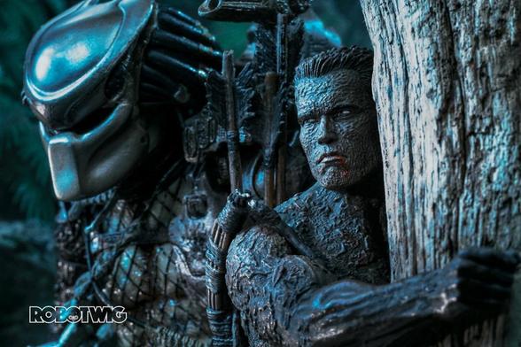 Dutch holds tightly to a tree whilst the the predator walks past him unable to see him as he's covered in mud