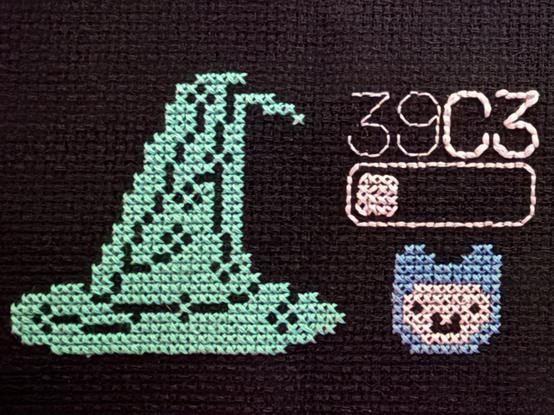 A cross stitch collage of the Haecksen logo (a mint green hat with circuits), the Jugend-Hackt-Logo (a smiling blue alpaca) and the 39c3 logo (39c3 with a sliding switch)
