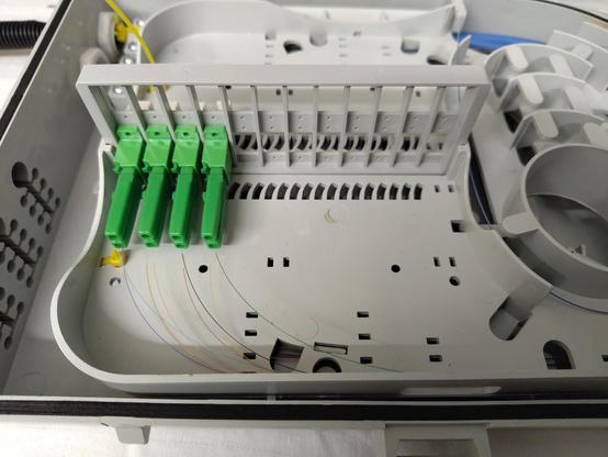 Nahaufnahme von den Innereien der Spleißbox, insbesondere von acht Glasfaser Klemmsteckern und die Fasern, die dort hinein führen.