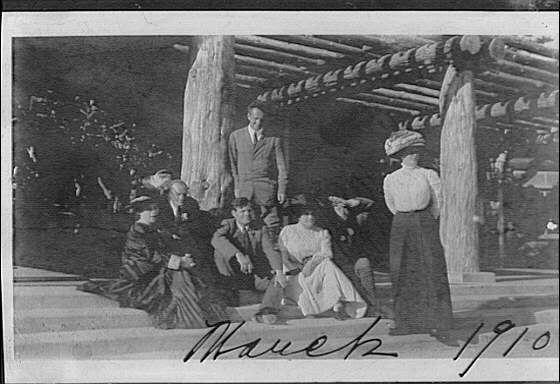 The image is a black and white photograph depicting eight individuals, likely from the early 20th century given their clothing style. They are gathered around what appears to be an outdoor wooden structure with pillars, possibly in California as indicated by the handwritten date "Washoe 1910." The group consists of both men and women dressed in period-appropriate attire such as suits, dresses, hats, and coats. A few individuals stand while others sit on steps or benches.

The photo is labeled "Arnold Genthe" at the bottom right corner, suggesting that Arnold Genthe was a person involved with this photograph possibly as its subject, photographer, or organizer of the gathering. The handwritten date in cursive script reads 'Washoe 1910,' which may refer to Washoe County, Nevada near Lake Tahoe.

The black and white tones provide historical context for the attire and architecture seen within the scene, indicative of early photographic techniques. It captures a moment from history with individuals dressed elegantly displaying their social status or leisurely pursuits in that era.

The photograph is noted as having "1 negative : safety ; 5 x 7 in. or smaller" dimensions suggesting it was likely created on film and printed using traditional methods for the time period mentioned.