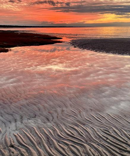 Photo of sunset over ocean bay as viewed from beach. Far side of bay is seen on horizon.Sand ripples in foreground. Reflections of red sunset in ripples and water.
I took this photo today just after the sun set on Cape Cod, Massachusetts.
