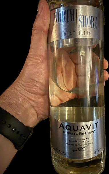 a poorly composed snapshot of me holding a half-empty bottle of Aquavit from North Shore Distillery