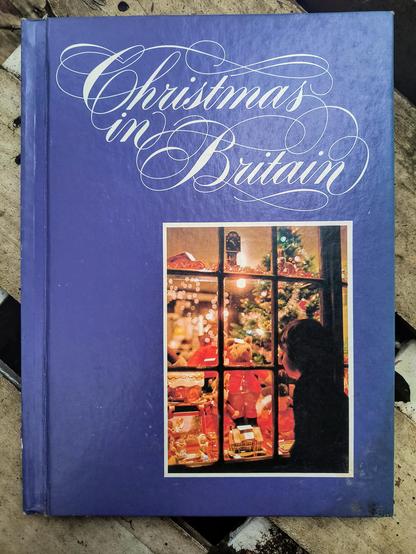 Cover of the book "Christmas in Britain", showing the title in an extremely fancy font, with a photo of a child looking into a brightly-colored Christmas display in a toyshop window. For what is the spirit of Christmas if not "looking from the cold, dark, outdoors at a warm and bright fantasy world of luxury that you cannot participate in."