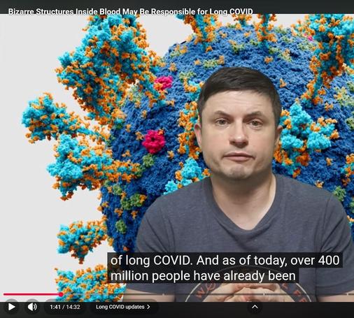 Description by Gemini Fast: A screenshot from a video titled "Bizarre Structures Inside Blood May Be Responsible for Long COVID." A man with short dark hair, wearing a blue t-shirt, is speaking, positioned in front of a massive, 3D visualization of a blue and orange spiky molecular structure (likely the SARS-CoV-2 virus).