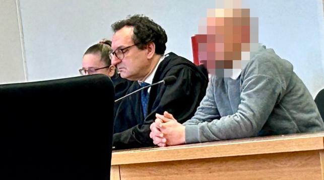 Drei Personen sitzen an einem Tisch, einer spricht in ein Mikrofon. Im Hintergrund eine Wand.