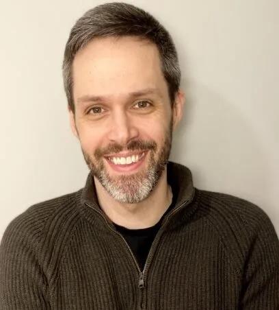 Headshot of Justin Clapp, PhD - beard, short hair, wearing a sweater - a linguistic and medical anthropologist who uses qualitative methods and social scientific theory to develop empirically tractable frameworks for examining medical ethics.