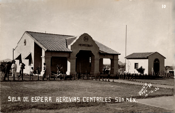 This black-and-white postcard view shows the early waiting area of Aerovías Centrales at Hermosillo, Sonora, Mexico, dated 1935. The main building is a single-story structure designed in a Spanish Colonial Revival style with stucco walls, a tiled gabled roof, and an arched central entrance supported by square columns. Above the entryway is the name Hermosillo along with an early aviation emblem. A smaller outbuilding with similar materials stands to the right, separated by a simple fenced walkway. Several men—some in military or aviation-style uniforms and others in civilian clothing—stand and sit near the front area, emphasizing the small, rural character of early regional air travel in northern Mexico. The landscape around the station is open and undeveloped, with low vegetation and distant hills visible beneath a clear sky. The caption at the bottom reads “SALA DE ESPERA AEROVIAS CENTRALES SON. MEX.”, identifying the view as the airline’s passenger waiting room.