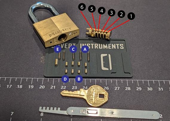 Master Lock 140 disassembled with the key, pins and springs, cylinder, and a comb tool
