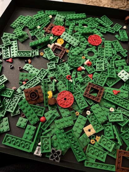 A large black tray filled with various pieces of LEGO, mainly in green with a few brown and red pieces mixed in.