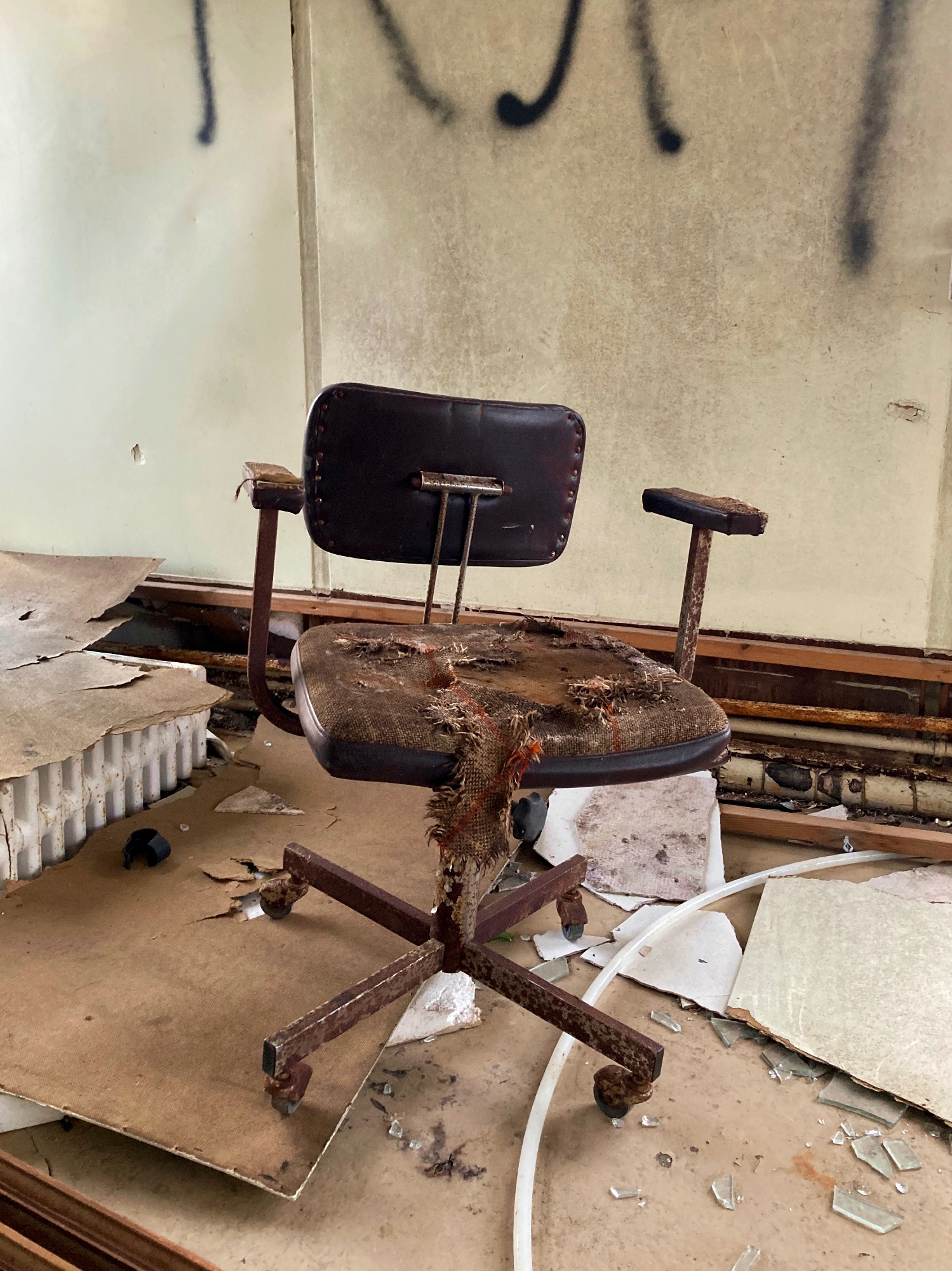 A very old, rusty office chair surrounded by trash.