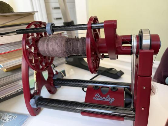 A starling espinner with a partially full bobbin. Left side, pink (day 2) and right, brownish purple, from day 1