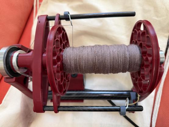 A bobbin on an espinner, partially full with a single of light pink