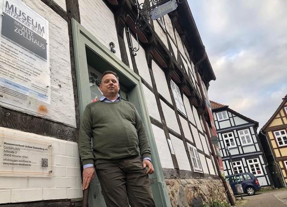 Mann vor einem Fachwerkhauseingang mit dem Schild "Museum Dassel" und Informationstexten. Gebäude mit dunklem Holz und weißen Füllungen.