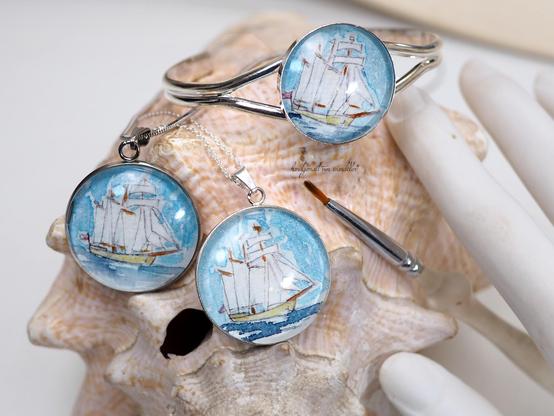 Hals -und Armschmuck, auf einer Muschel fotografiert; jeweils mit handgemaltem Motiv Segelschiff