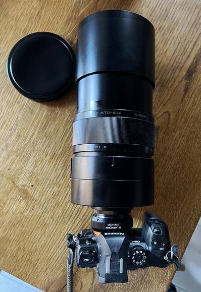 Olympus Om-1 con MC1000A agganciato, posata su un tavolo. La lente è 10 volte le dimensioni del corpo macchina.