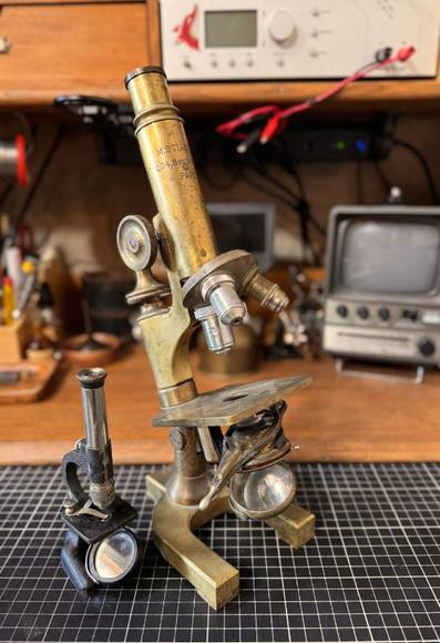 Two antique microscopes side by side, one much smaller than the other