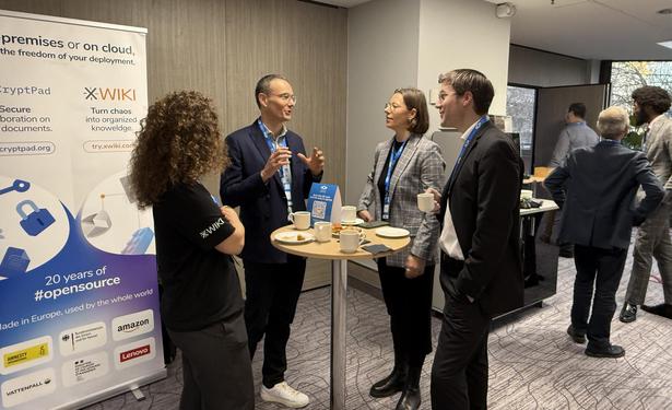 Event attendees speaking and networking at the OpenProject and XWiki booth during OSXP 2025, with banners promoting open-source collaboration.
