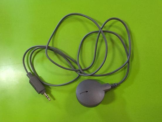A round, dark gray microphone with a thin cord and a tip ring sleeve connector with a mini DIN style housing, lying on a bright green background.
