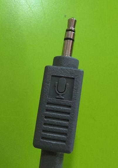 A closeup of a tip ring sleeve connector with a dark gray plastic housing with the microphone symbol molded into the plastic. On a bright green background.