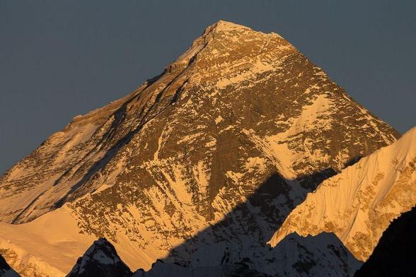 Colour photograph of Mount Everest (Sagarmatha / Chomolungma; 8850m) as seen at sunset from Gokyo Ri. Everest Base Camp Trek, Everest Region, Solukhumbu, Nepal. The  partially glacier and snow covered mountain is orange in colour and looks warm lit by the warm rays of the setting sun. © Radek Kucharski / pics.born2trek.com