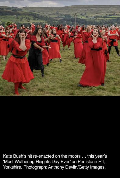 A large group of people in red outfits performing in a grassy field on Penistone Hill, Yorkshire, during the annual 'Most Wuthering Heights Day Ever' event, celebrating Kate Bush's song.