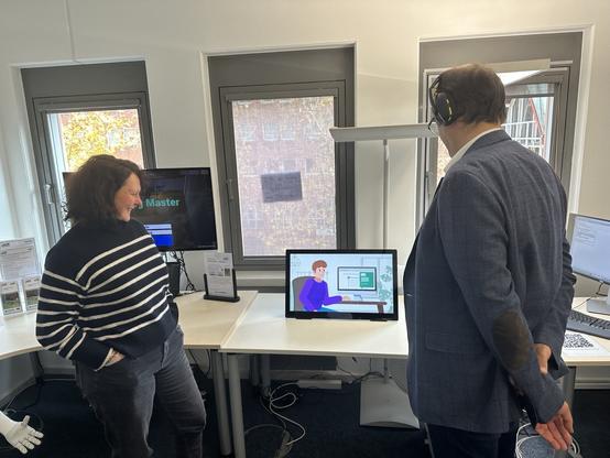 Anne Hennig (SECUSO) und Prof. Stefan Katzenbeisser stehen im Showroom von SECUSO und sehen sich ein Informationsvideo über Website-Hackings an.