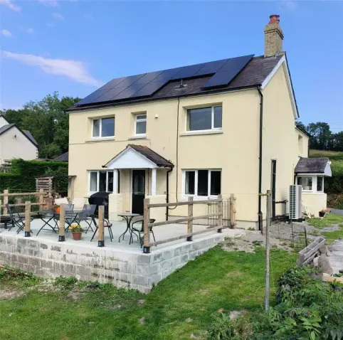 Cream-coloured detached house with solar panels and raised patio seating area in rural Carmarthenshire.
