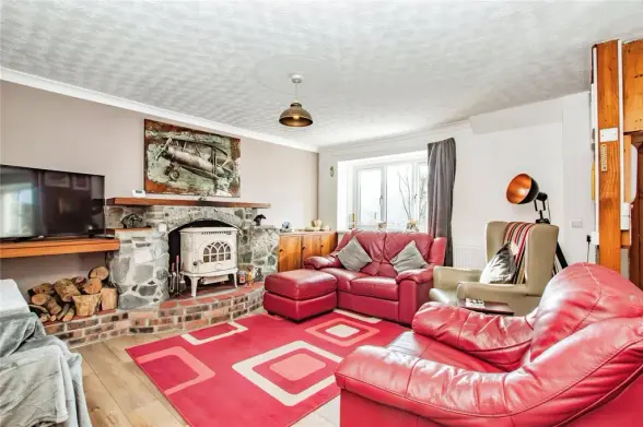 Living room with red leather furniture, stone fireplace, wood-burning stove and vintage decor.