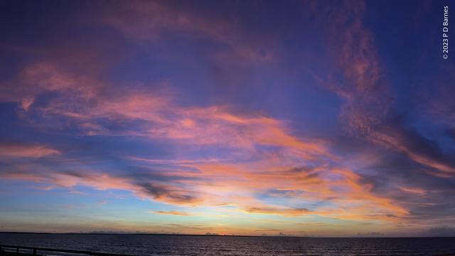 Sunset. Drifts of wispy clouds over the sea, all lit bright pink by the just-set sun against a startling blue sky.