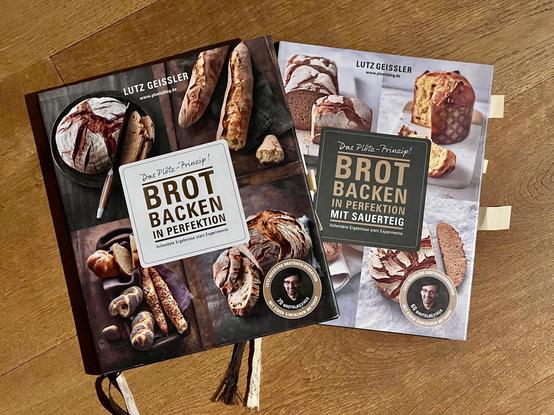 Auf einem Holzboden liegen zwei Bücher mit dem Titel "Brot backen in Perfektion" von Lutz Geißler