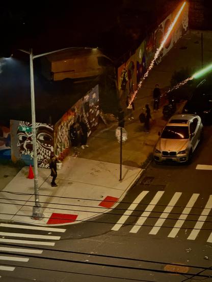 Teenage kids set of amateur fireworks in the street at night time on the 4th of July in Astoria, Queens. The fireworks appear as bright red and green flashes of light on this shot.