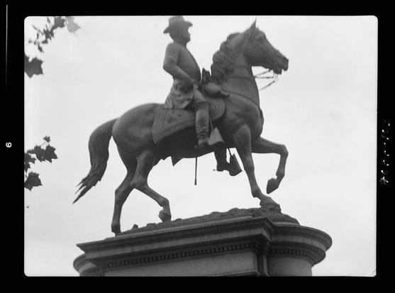 The image depicts a monochrome photograph of an equestrian statue, showing the upper part of the sculpture which includes a horse and rider. The figure appears to be that of a man dressed in what seems like early 19th-century military attire, complete with a helmet-like hat. He is seated on top of a rearing horse, suggesting action or readiness for battle.
The statue is mounted atop a pedestal which has classical architectural elements such as fluted columns at the bottom edge and ornamental detailing along its sides. The background features some foliage that provides context to the height at which this monument stands but does not offer any specific details about location.
This photograph may be part of historical documentation, possibly from early 20th-century America based on the caption mentioning "Equestrian statues in Washington, D.C." during a specified period. Arnold Genthe (1869-1942) is credited as the photographer or associated with this image, which suggests that it may have been taken by an individual known for documenting significant historical figures and events.
The specific statue's identity isn't disclosed here to maintain objectivity; however, equestrian statues are often erected in public spaces to commemorate notable military leaders or important personalities. The details of the attire on both horse and rider suggest a figure likely linked with martial prowess or leadership from that era.