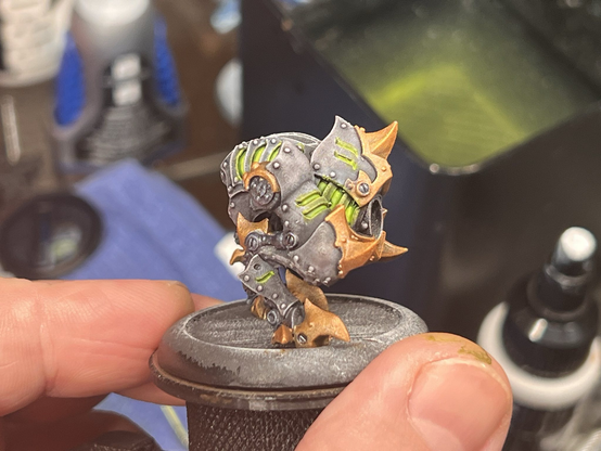 A painted miniature of a Cryx bonejack from Warmachine. The creature in question could be described as a bipedal mechanical chicken, with the magnetized head and weaponry missing from the photo. The armor plating on the bonejack is a lighter grey / brown, with the knees, spurs, and clawed toes in a shining gold. Numerous vents cover the surface, where one can see the sickly green glow of undead soul juice powering the small menace from inside. 

This second photo shows the right side of the jack, unsurprisingly similar to the left side.