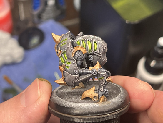 A painted miniature of a Cryx bonejack from Warmachine. The creature in question could be described as a bipedal mechanical chicken, with the magnetized head and weaponry missing from the photo. The armor plating on the bonejack is a lighter grey / brown, with the knees, spurs, and clawed toes in a shining gold. Numerous vents cover the surface, where one can see the sickly green glow of undead soul juice powering the small menace from inside.

This third photo shows a very clear side view of the jack, where one is more able to see the vents along the back flank.
